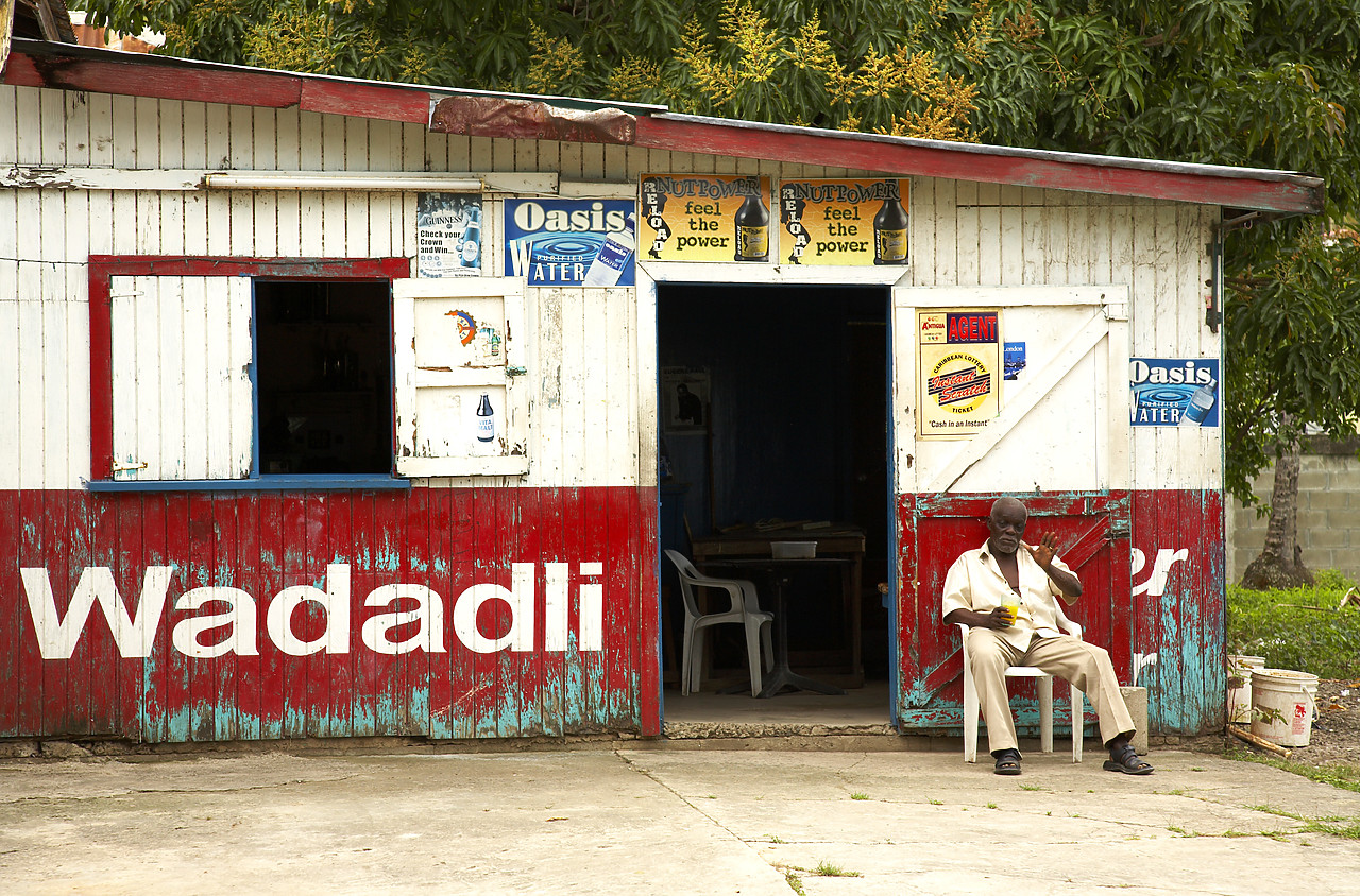 #070042-1 - Local Man Sitting in front of Colourful Building, Antigua, Caribbean